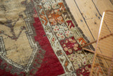 Close-up of vintage Melas rug's tattered side, textured pile, and beige, red, orange tones.