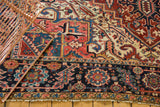 Persian Heriz carpet corner showing navy floral border, red geometric field, and even pile wear.