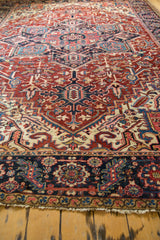 Vintage Heriz carpet: cherry red, navy geometric field, wide serrated border, and soft worn pile.
