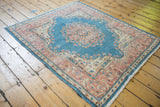 Distressed Kerman rug's sky blue field, intricate pink floral border, and fringed corner.