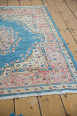 Distressed Kerman rug corner: sky blue field, pink curvilinear border, low pile, fringe.