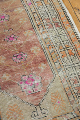 Distressed Oushak rug detail showing dusty cochineal field, pink floral motifs, and geometric border.