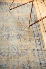 Textured distressed Oushak rug with faded blue pattern, even wear, and secured edge.