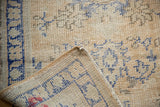 Distressed Oushak rug corner, worn ivory-beige pile, cobalt blue motifs, visible hand-knotted foundation.
