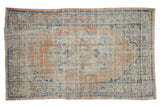 Distressed vintage Turkish Oushak rug with faded apricot medallion, laurel floral motif, and blue accents.