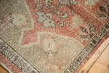Distressed vintage Oushak rug pile, showing faded dusty rose, beige, and intricate border.