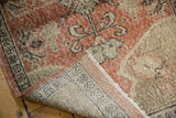 Corner of distressed Oushak rug revealing faded floral pattern and hand-knotted reverse.