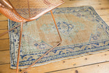 Oushak rug corner: geometric cobalt border, pale apricot field, and characteristic wear.