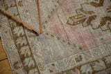 Distressed Oushak rug texture with faded dusty rose, beige patterns and visible wear.