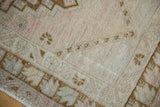 Distressed pile of a vintage Oushak rug with faint foundation, showing muted dusty rose and beige tones.