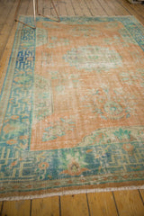 Distressed Oushak rug corner showing faint foundation, faded tangerine, and seafoam green geometric border with fringe.
