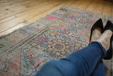Distressed Oushak runner's worn pile texture with faded blush, blue, and orange floral motifs.