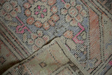 Folded distressed Oushak rug showing worn texture and faded orange, blue, pink patterns.