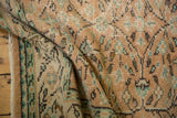 Textured fold of vintage Oushak carpet showing distressed apricot, mint, and charcoal vinery.