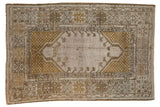 Distressed Vintage Melas rug with an open field, germinating floral motifs, and geometric borders in beige and bronze.