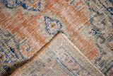 Distressed vintage Oushak rug corner revealing hand-knotted foundation with rust, blue, and ivory colors.
