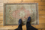 Distressed Oushak rug corner showing worn pile, dusty rose, pale mint green, meandering vine border.