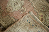 Folded corner of vintage distressed Oushak rug, showing worn pile, visible foundation, dusty rose, and mint.