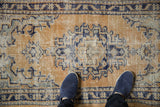 Distressed Oushak rug texture underfoot, showing pale gold, cobalt blue, and visible foundation.