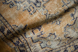Distressed Oushak rug detail with faded dusty gold and cobalt blue on a textured, low pile.