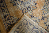 Distressed vintage Oushak rug corner, showing worn gold and ivory pile, foundation, and secured edge.