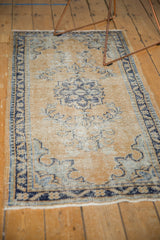 Distressed Oushak rug corner with fringed edge, featuring faded gold and blue tones.