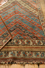 Detail of the antique Kurdish rug's wide camel border, patterned guard band, and original fringed edge.