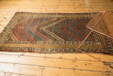 Antique Kurdish rug corner displaying parallel cherry red and sky blue floral stripes with a wide camel border.
