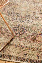 Antique Kerman runner's edge, showing machine binding, worn pile, visible foundation, and floral motifs.