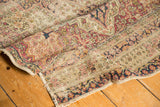 Folded antique Kerman runner fragment, revealing worn hand-knotted pile, ivory, red, and navy patterns.