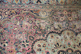Close-up of vintage Meshed carpet showing faded plum and blue floral vinery, low pile with foundation visible.