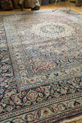 Corner of vintage Meshed rug showing faded plum, pale blue floral vinery, and low pile.