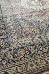 Angled view of a vintage Meshed carpet's intricate floral borders and muted blue-plum vinery.