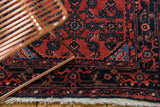 Corner of vintage Persian Engelas rug, showcasing navy samovar border, red Herati field, and fringe.
