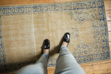 Distressed beige Oushak rug with low pile, visible foundation, and blue border.