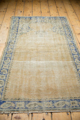 Distressed vintage Oushak rug corner, with worn beige field and faded blue border.