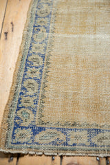 Distressed texture of a beige Oushak rug with visible knot heads and blue geometric border.