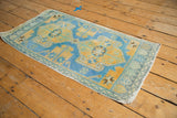 Distressed Oushak rug corner, showcasing sky blue, saffron yellow, and teal border pattern with wear.
