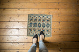Feet on a distressed Oushak square mat with repeating teal and ivory floral patterns.