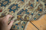 Hand reveals texture of vintage distressed Oushak rug, with teal, ivory, and brown florals.