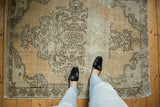 Distressed Oushak rug pile texture with worn medallion and soft beige colors.
