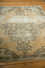 Distressed Oushak rug: scalloped vinery pattern, even wear to knot heads, sand field, and fringe.