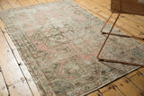 Distressed Oushak rug corner with staggered square motif in dusty rose, ivory, and green.