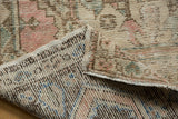 Folded vintage distressed Oushak rug highlighting worn pink and green pile, revealing hand-knotted foundation.