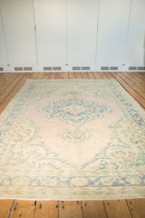 Distressed vintage Oushak rug corner showing pale dusty pink field, faded denim blue curvilinear spandrel.
