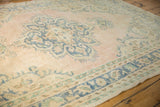 Corner detail of distressed vintage Oushak rug with pale pink field and blue border.