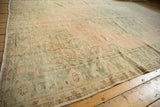 Distressed Oushak carpet corner with faded seafoam green, dusty pink, and even wear.