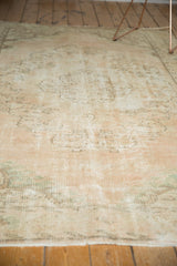 Distressed pile of vintage Oushak rug, revealing faded blush, ivory, and seafoam green patterns with wear.