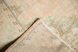 Distressed vintage Oushak rug showing worn pile with pale blush, green, and hand-knotted foundation.