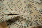Distressed Melas rug texture, worn geometric motifs in beige, sand, and seafoam green.